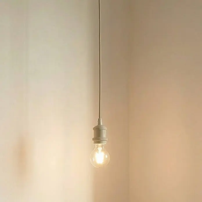 Lindby Pendelleuchte Hattie - creme / amber, beige, E27 - Eine einfache Pendelleuchte mit einer leuchtenden, klaren Glühbirne, die warmes Licht abstrahlt, hängt von der Decke.