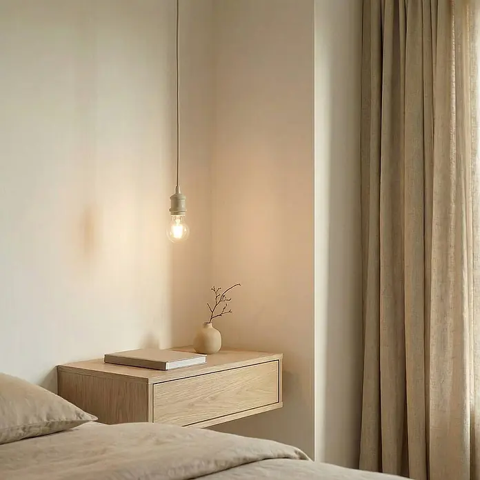 Lindby Pendelleuchte Hattie - creme / amber, beige, E27 - Eine schlichte Pendelleuchte mit freiliegender Glühbirne hängt in einer Schlafzimmerecke über einem hellen schwebenden Nachttisch aus Holz.