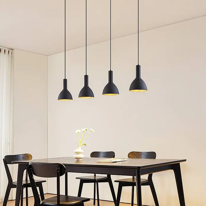 Arcchio Pendelleuchte Cosmina - schwarz, Schwarz, gold, E27 - Vier schwarze Pendelleuchten mit goldenem Interieur hängen über einem dunklen Esstisch aus Holz.