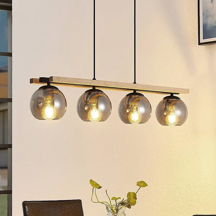 Lindby Pendelleuchte Enrique - L x B x H: 90 x 15 x 13 cm, alu / grau / zink, rauchgrau, eiche hell, Schwarz, E27 - Pendelleuchte mit Holzbalken und vier beleuchteten Rauchglas-Kugelschirmen über einem Esstisch.