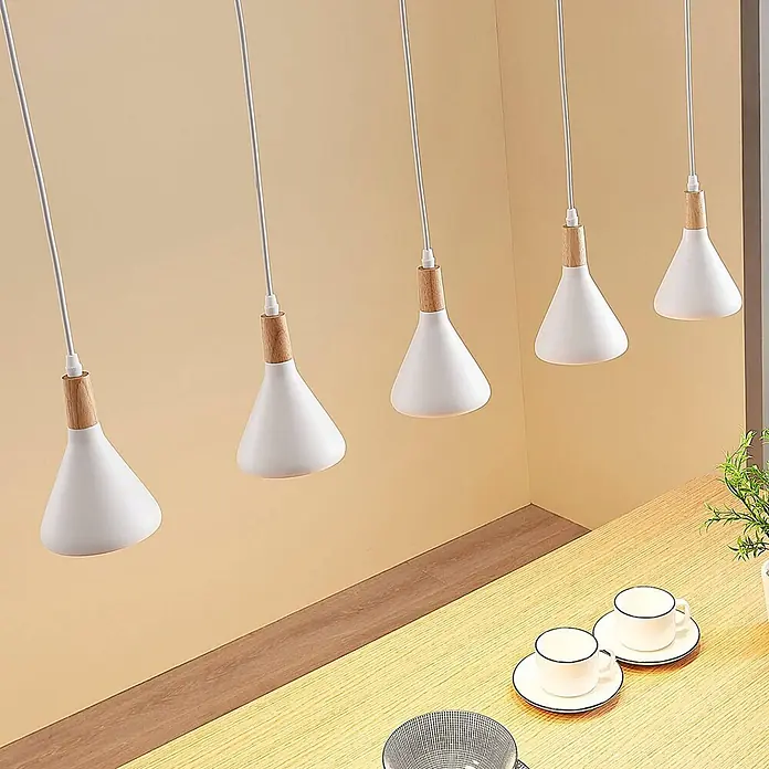 Lindby Pendelleuchte Arina - weiß / opal, weiß, holz hell, E14 - Fünf weiße und hölzerne kegelförmige Pendelleuchten hängen über einer hellen Holztheke.