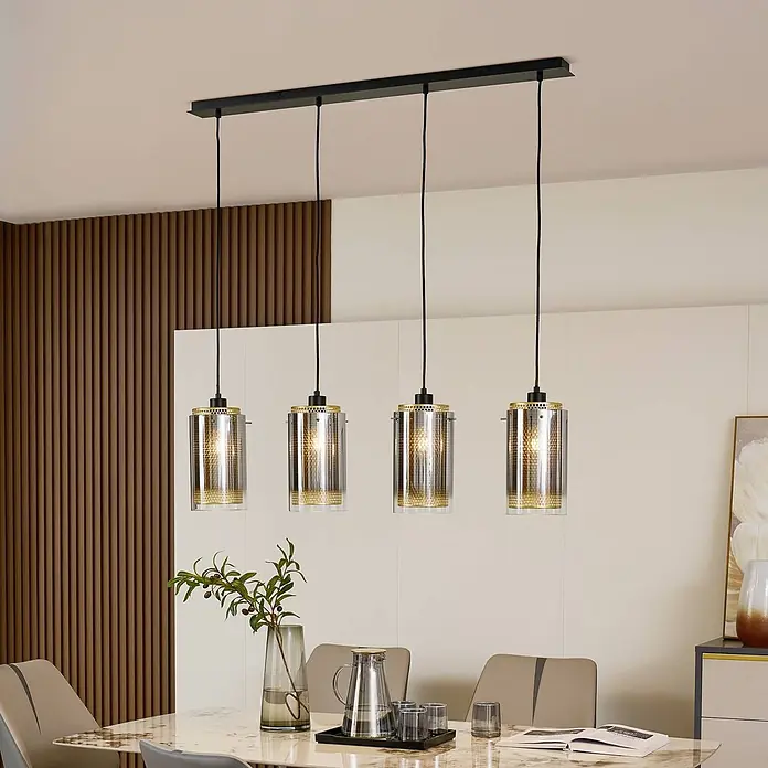 Lucande Pendelleuchte Sterzy - L x B x H: 105 x 15 x 28,5 cm, alu / grau / zink, anthrazit, gold, E27 - Eine 4-flammige lineare Pendelleuchte mit schwarzem Balken, klaren Glasschirmen und goldfarbenen Lochmetallakzenten über einem Esstisch.