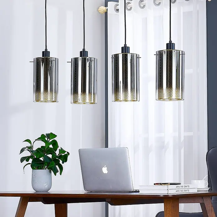 Lucande Pendelleuchte Sterzy - L x B x H: 105 x 15 x 28,5 cm, alu / grau / zink, anthrazit, gold, E27 - Vier zylindrische Pendelleuchten mit klaren Außenschirmen und goldenen Wabenmustern innen, über einem Schreibtisch mit Laptop und Pflanze.