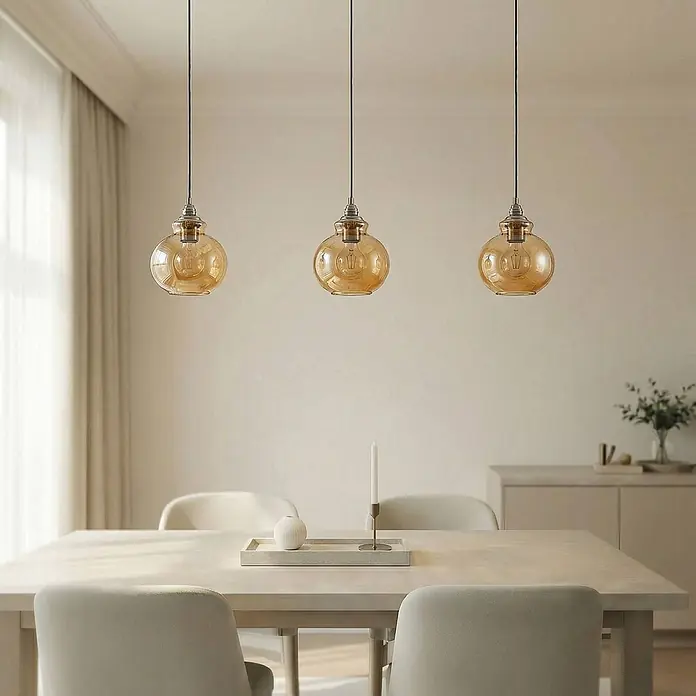 Lindby Pendelleuchte Tymoni - creme / amber, amber, altmessing, E27 - Drei Pendelleuchten aus bernsteinfarbenem Glas hängen elegant über einem Esstisch und beleuchten den Raum.
