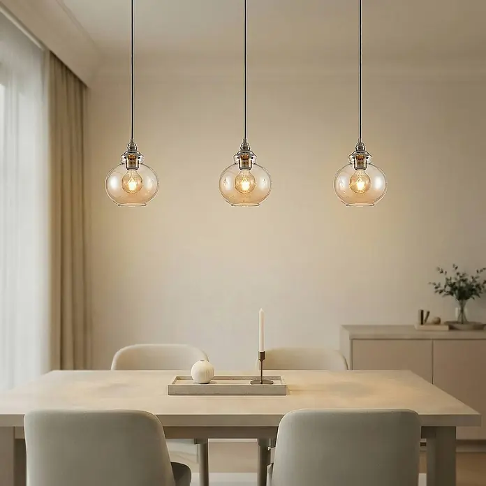 Lindby Pendelleuchte Tymoni - creme / amber, amber, altmessing, E27 - Drei Pendelleuchten mit bernsteinfarbenen Glaskugeln hängen über einem Esstisch und spenden warmes Licht.