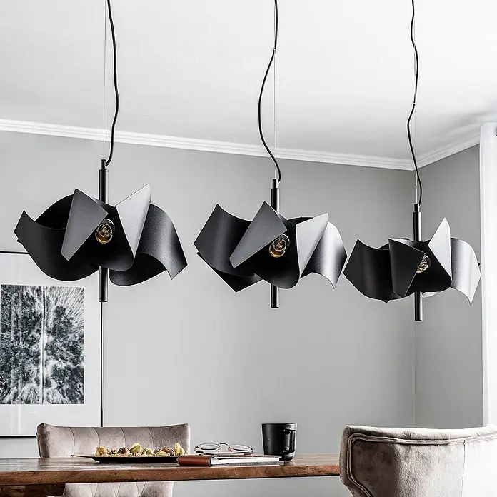 Lucande Pendelleuchte Imron - L x B x H: 142 x 40 x 35 cm, schwarz, sandSchwarz, E14 - Drei schwarze Pendelleuchten mit gefalteten, wellenförmigen Schirmen über einem Esstisch aus Holz.