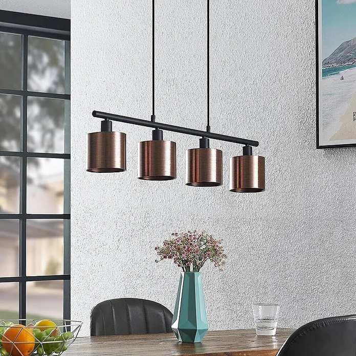 Lindby Pendelleuchte Joudy - L x B x H: 75 x 12 x 11 cm, bronze / altmessing, bronze dunkel, Schwarz matt, E14 - Vierflammige Pendelleuchte mit kupferfarbenen zylindrischen Schirmen und schwarzer Stange über einem Holztisch.