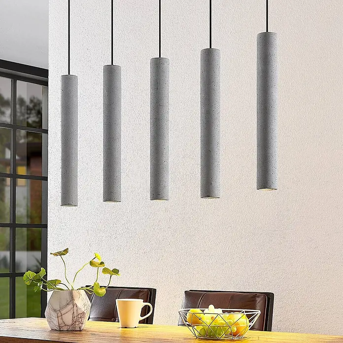 Lindby Pendelleuchte Concretto - alu / grau / zink, grau, GU10 - Fünf zylindrische Pendelleuchten aus grauem Beton hängen über einem Esstisch und beleuchten den Raum mit warmem Licht.