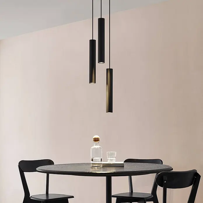 Lindby Pendelleuchte Joffrey - L x B x H: 24 x 24 x 40 cm, schwarz, Schwarz sand, GU10 - Drei schwarze zylindrische Pendelleuchten über einem dunklen Holztisch.