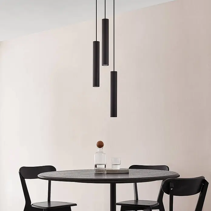 Lindby Pendelleuchte Joffrey - L x B x H: 24 x 24 x 40 cm, schwarz, Schwarz sand, GU10 - Drei schwarze zylindrische Pendelleuchten hängen in verschiedenen Höhen über einem dunklen Esstisch.
