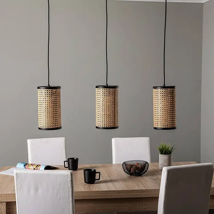Lindby Pendelleuchte Yaelle - L x B x H: 92 x 15 x 28 cm, Holz hell, holz hell, E27 - Drei zylindrische Rattan-Pendelleuchten mit schwarzen Akzenten hängen über einem Esstisch aus Holz.