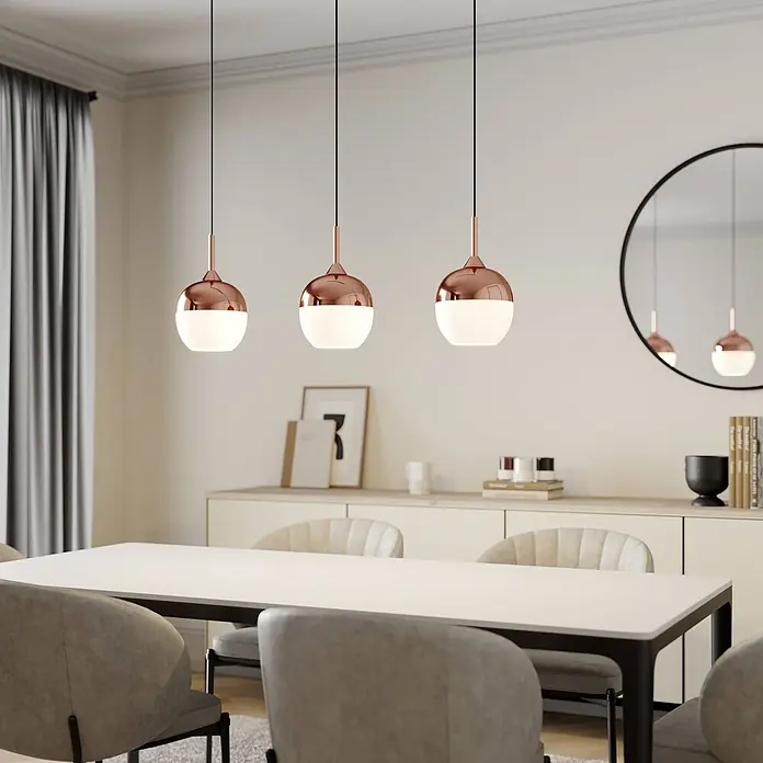 Lindby Pendelleuchte Rangina - kupfer, Kupfer, weiß, E27 - Drei Pendelleuchten aus Roségold und weißem Glas hängen über einem Esstisch.