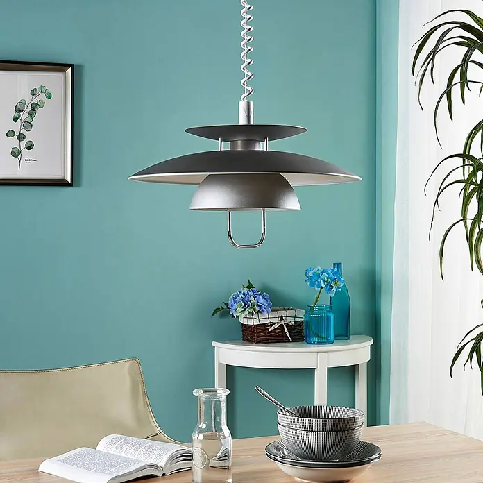 Lindby Pendelleuchte Nadija - L x B x H: 43 x 43 x 28 cm, alu / grau / zink, grau, weiß, E27 - Eine moderne, mehrstufige graue Pendelleuchte hängt über einem Holztisch in einem Raum mit tealfarbener Wand.