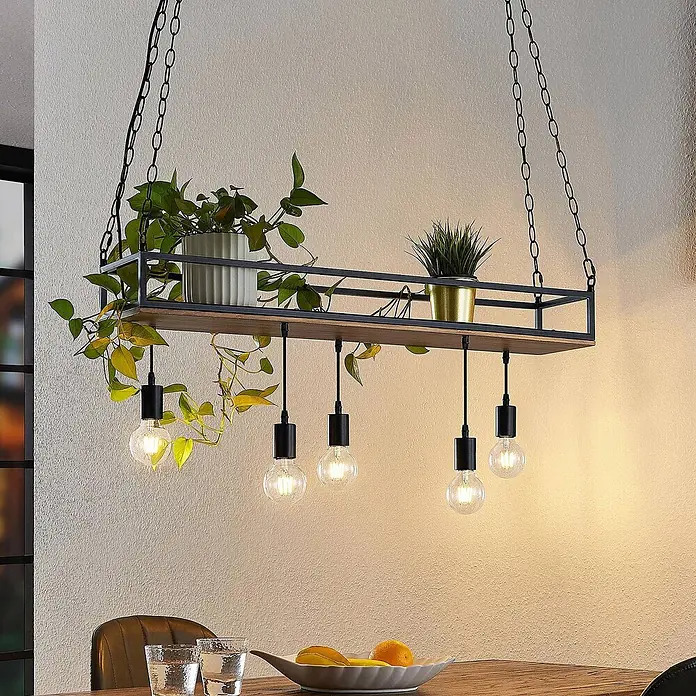Lindby Pendelleuchte Kirista - L x B x H: 100 x 20 x 15 cm, Schwarz, kiefer dunkel, E27 - Hängelampe im Industriestil mit schwarzem Metallrahmen, Holzablage, Pflanzen und fünf sichtbaren Glühbirnen über einem Esstisch.