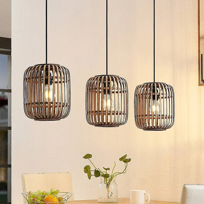 Lindby Pendelleuchte Canyana - L x B x H: 105 x 21,5 x 25 cm, Holz hell, natur, E27 - Drei natürliche Bambus-Pendelleuchten mit sichtbaren Glühbirnen hängen über einem Esstisch.