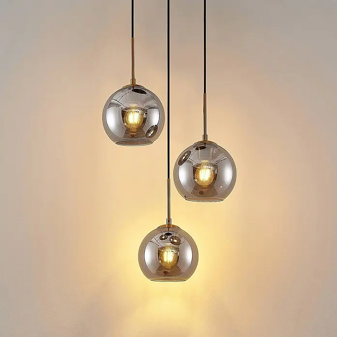 Lindby Pendelleuchte Jurian - L x B x H: 32 x 32 x 17,5 cm, alu / grau / zink, bronze, rauchgrau, E27 - Drei beleuchtete Pendelleuchten mit rauchgrauen Glaskugeln und Messingakzenten.