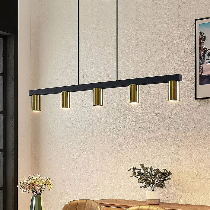 Lindby Pendelleuchte Baliko - messing, Schwarz, GU10 - Schwarze lineare Pendelleuchte mit fünf messingfarbenen zylindrischen Strahlern über einem Holztisch.