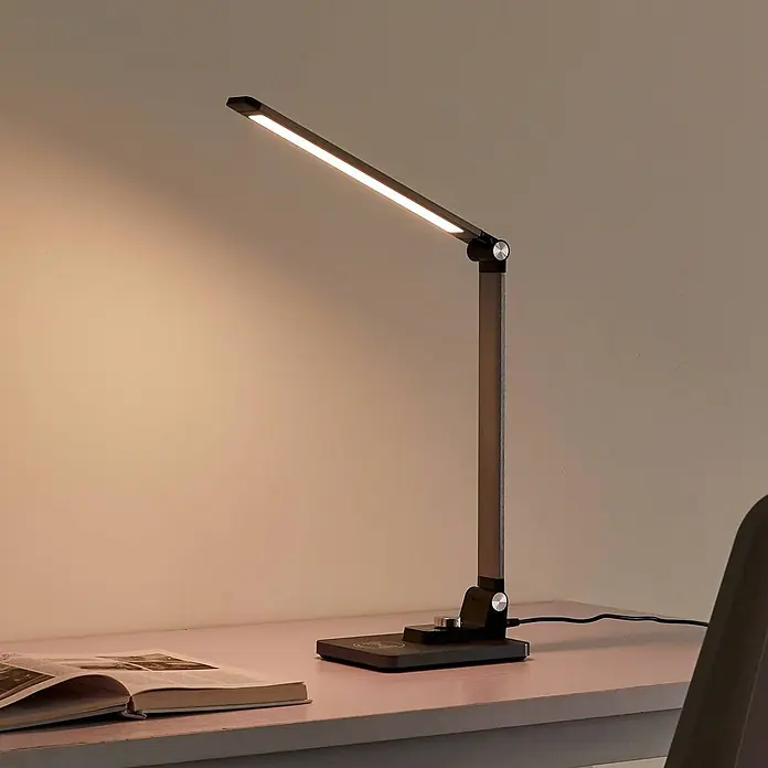 Lindby Tischleuchte Valtaris - L x B x H: 35,6 x 13,7 x 43,1 cm, alu / grau / zink, alu / grau / zink - Moderne dunkelgraue Schreibtischlampe mit verstellbarem Arm und warmem LED-Licht, beleuchtet ein offenes Buch auf einem Schreibtisch.