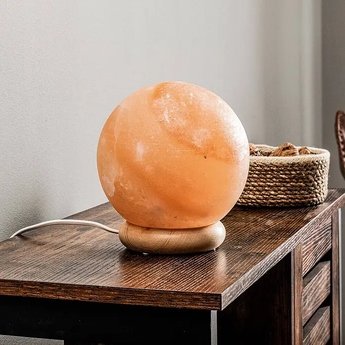 Envostar Tischleuchte Harmony - rot, E14 - Kugelförmige orangefarbene Himalaya-Salzlampe auf rundem Holzsockel, mit weißem Kabel, auf einem dunklen Holztisch neben einem Weidenkorb.