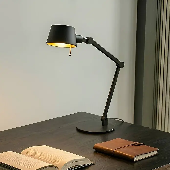 Lucande Tischleuchte Silka - schwarz, schwarz, E27 - Mattschwarze Schreibtischlampe mit goldener Innenseite beleuchtet einen dunklen Holzschreibtisch mit offenem Buch und Ledernotizbuch.
