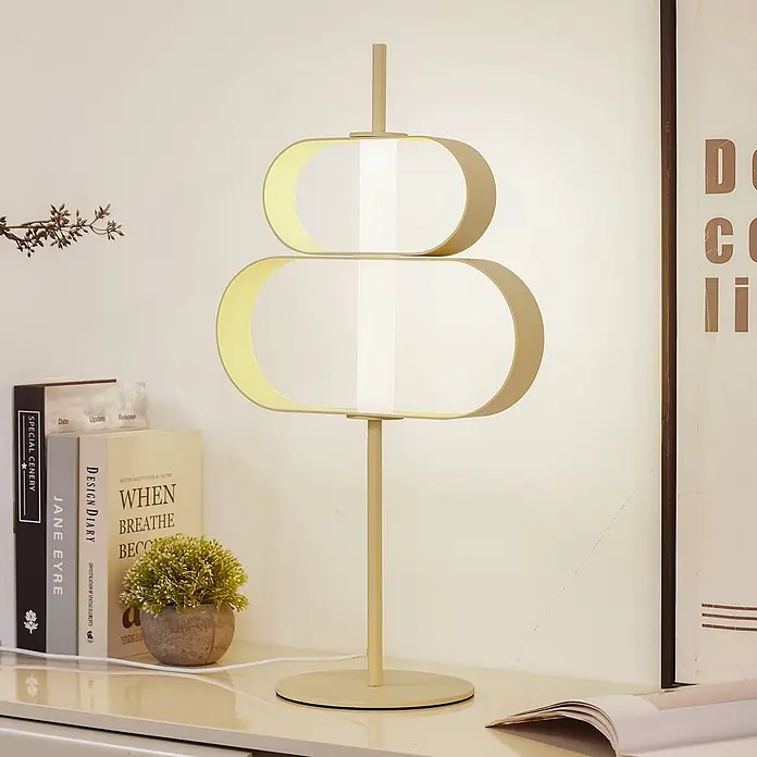 Lucande Tischleuchte Audrina - creme / amber - Eine moderne, goldfarbene Tischlampe mit zwei horizontalen ovalen Diffusoren, die sanftes Umgebungslicht auf einem Schreibtisch spendet.
