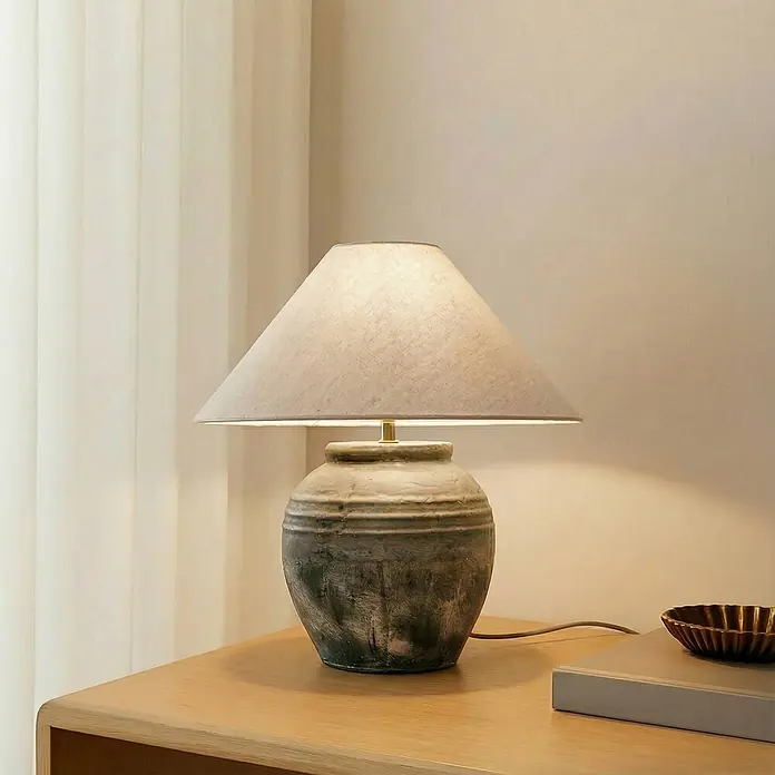 Lucande Tischleuchte Thalorin - braun / rost, E27 - Tischlampe mit strukturierter Keramikbasis und hellem Stoffschirm, spendet Licht auf einem Holztisch.