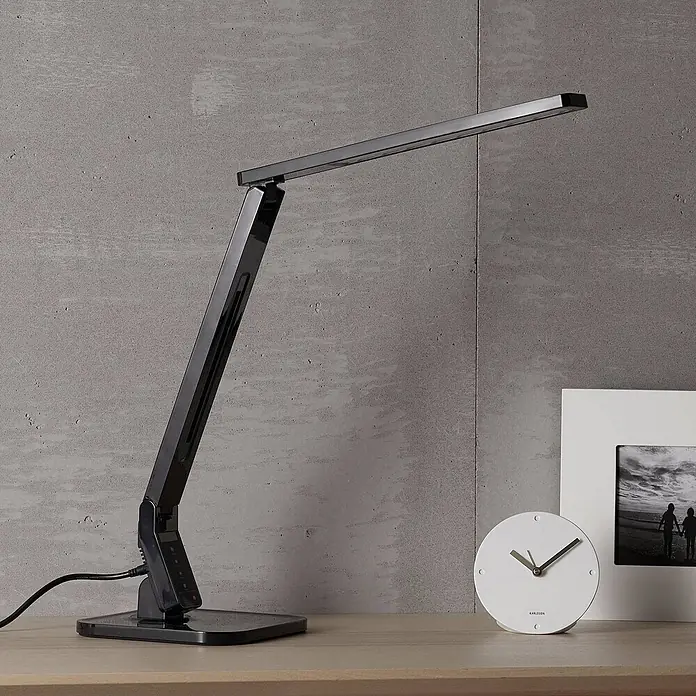 Lindby Tischleuchte Eleni - L x B x H: 18 x 17,2 x 45 cm, schwarz, schwarz - Elegante schwarze LED-Schreibtischlampe mit verstellbaren Armen und Touch-Bedienung auf einem Schreibtisch neben einer Uhr und einem Bilderrahmen.