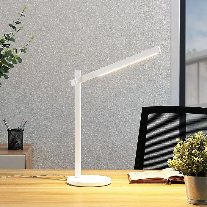 Lindby Tischleuchte Loretta - L x B x H: 40,8 x 17 x 43 cm, weiß / opal, weiß / opal - Weiße moderne LED-Schreibtischlampe leuchtet auf einem Holzschreibtisch, neben einem Bürostuhl und einer Pflanze.