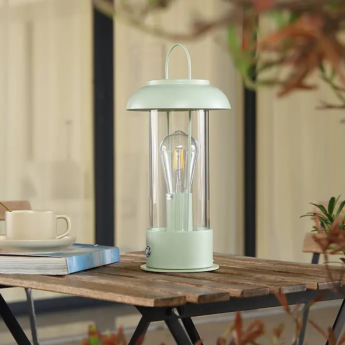 Lindby Tischleuchte Yvette - L x B x H: 17 x 17 x 36,4 cm, grün, klar / transparent, E27 - Hellgrüne Retro-Laterne mit Edison-Glühbirne, als Tischlampe auf einem Holztisch im Freien.
