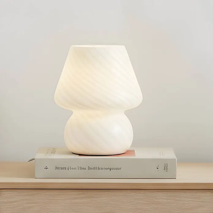 Lindby Tischleuchte Andriana - weiß / opal, weiß / opal, E14 - Weiße Pilz-Tischlampe aus Glas mit Swirl-Muster, auf einem Buch auf heller Holzoberfläche.
