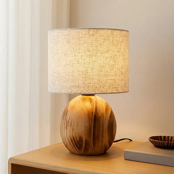 Lindby Tischleuchte Mayumi - L x B x H: 22 x 22 x 31 cm, Holz hell, alu / grau / zink, E27 - Tischlampe mit kugelförmigem Holzsockel und natürlichem Stoffschirm, spendet warmes Licht auf einer Holzoberfläche.