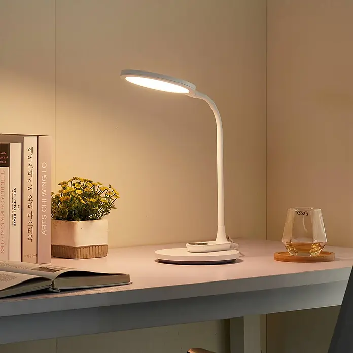 Lindby Tischleuchte Valtaria - L x B x H: 28,8 x 17 x 38,1 cm, weiß / opal, weiß / opal - Eine weiße, moderne LED-Schreibtischlampe mit flexiblem Schwanenhals beleuchtet einen Schreibtisch mit Büchern und einer Pflanze.