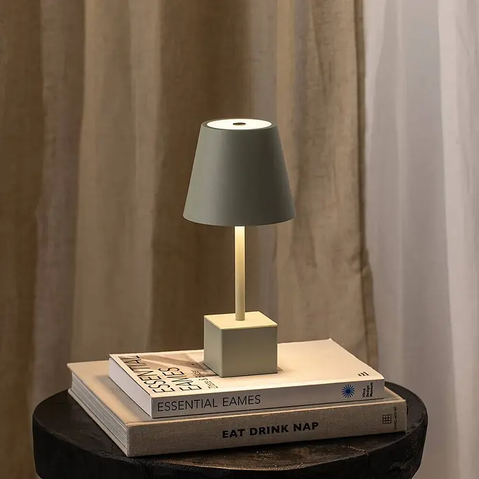 Lindby Tischleuchte Janea - grün, grün - Beleuchtete salbeigrüne Tischlampe auf einem Stapel Bücher auf einem dunklen Holzhocker.