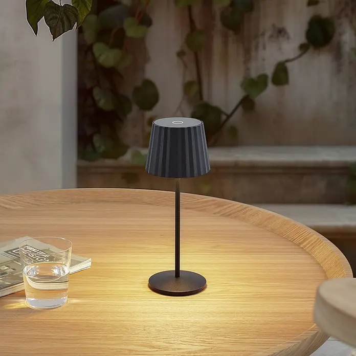 Lindby Tischleuchte Esali - L x B x H: 11 x 11 x 28,5 cm, schwarz, schwarz - Dunkelgraue Tischleuchte mit plissiertem Schirm und rundem Sockel, spendet warmes Licht auf einem Holztisch.