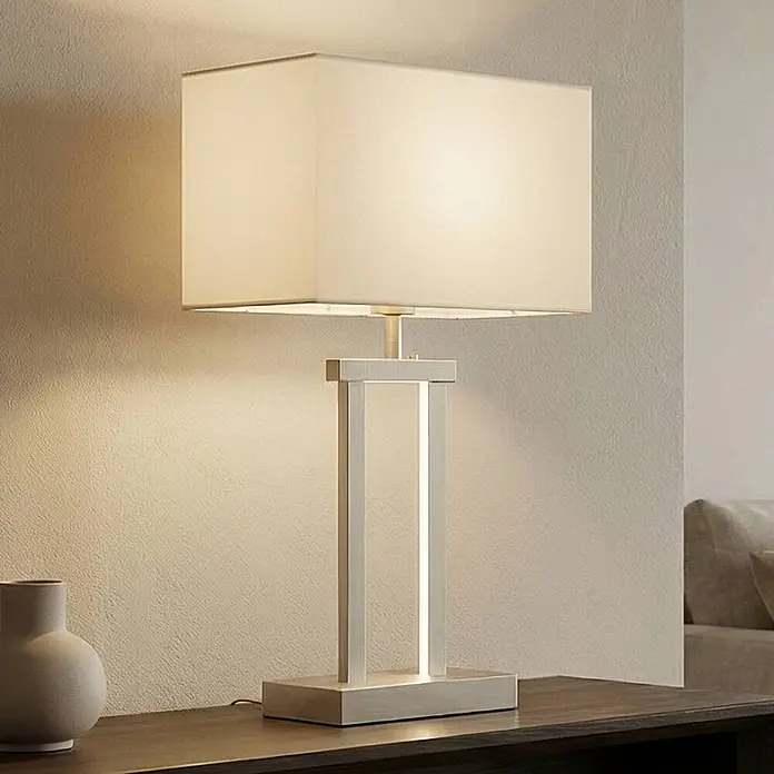 Lindby Tischleuchte Sigurd - alu / grau / zink, weiß / opal, E27 - Moderne Tischlampe mit rechteckigem hellem Stoffschirm und gebürstetem silbernem Metallsockel auf einer dunklen Holzoberfläche.