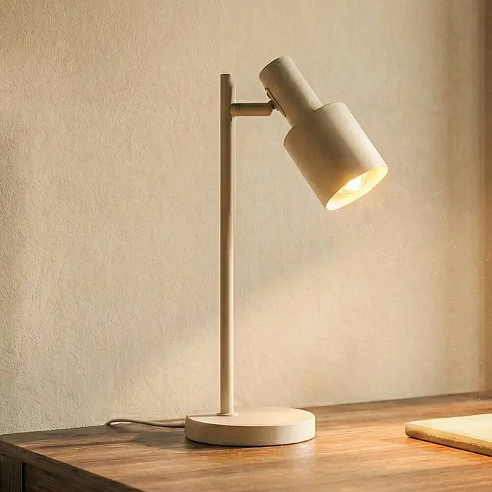 Lindby Tischleuchte Ovelia - creme / amber, creme / amber, E27 - Moderne beigefarbene Schreibtischlampe mit verstellbarem Kopf, beleuchtet einen Holzschreibtisch vor einer hellen strukturierten Wand.
