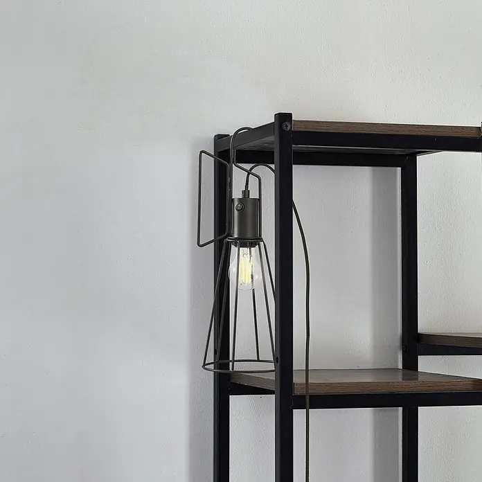 Lindby Tischleuchte Tharion - L x B x H: 15,4 x 15,4 x 42,6 cm, schwarz, E27 - Dunkelgraue Käfig-Handleuchte mit sichtbarer Filamentbirne, hängt an einem schwarzen Metall-Holz-Regal.