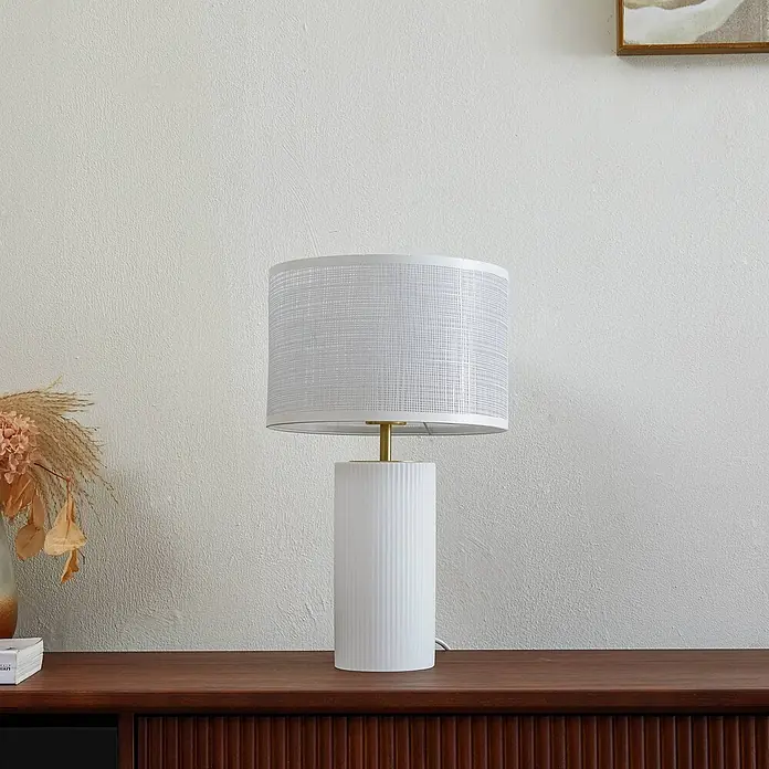 Lindby Tischleuchte Sorscha - L x B x H: 26 x 26 x 43 cm, weiß / opal, weiß / opal, E27 - Weiße geriffelte Keramik-Tischlampe mit Messingakzent und weißem strukturiertem zylindrischem Schirm, auf einem Sideboard aus Holz.