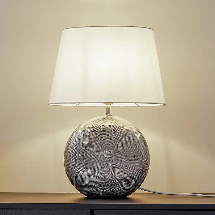 Lindby Tischleuchte Florentino - L x B x H: 35 x 23,5 x 48,5 cm, alu / grau / zink, weiß / opal, E27 - Tischlampe mit weißem Stoffschirm und rundem, texturiertem Metallsockel auf einem dunklen Holztisch.