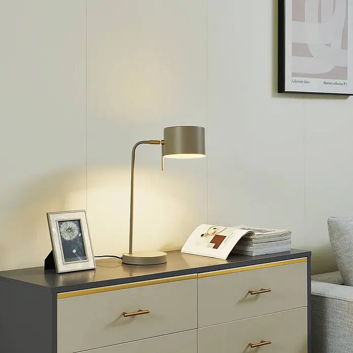 Lindby Tischleuchte Kaida - L x B x H: 30 x 15 x 43,5 cm, braun / rost, braun / rost, E27 - Matte graue Tischlampe mit Messingakzenten, die eine Kommode beleuchtet. Die Lampe strahlt ein warmes Licht aus.
