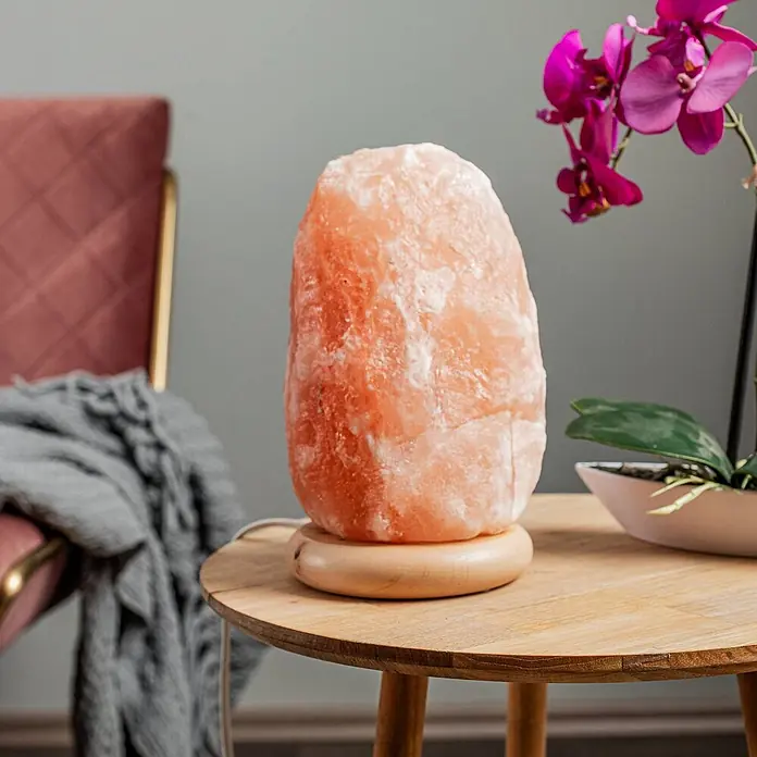 Envostar Tischleuchte Harmony - rot, E14 - Eine leuchtende Himalaya-Salzlampe mit einem natürlichen rosa-orangen Kristall und einem runden Holzsockel auf einem hellen Holztisch.