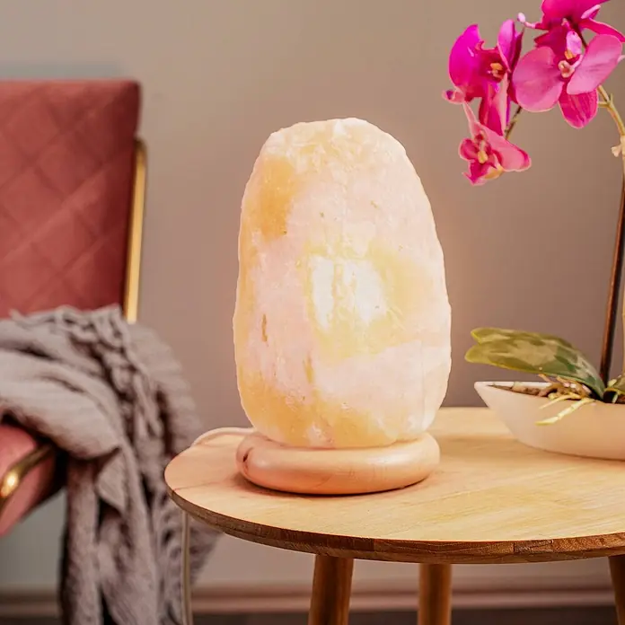 Envostar Tischleuchte Harmony - rot, E14 - Eine leuchtende Himalaya-Salzlampe mit natürlicher, unregelmäßiger Form und rundem Holzsockel steht auf einem hellen Holztisch.