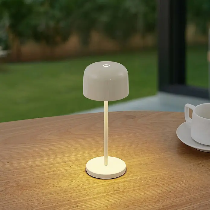 Lucande Tischleuchte Quill - creme / amber, creme / amber - Eine hellbeige, moderne tragbare Tischlampe mit warmem Licht auf einem Holztisch.
