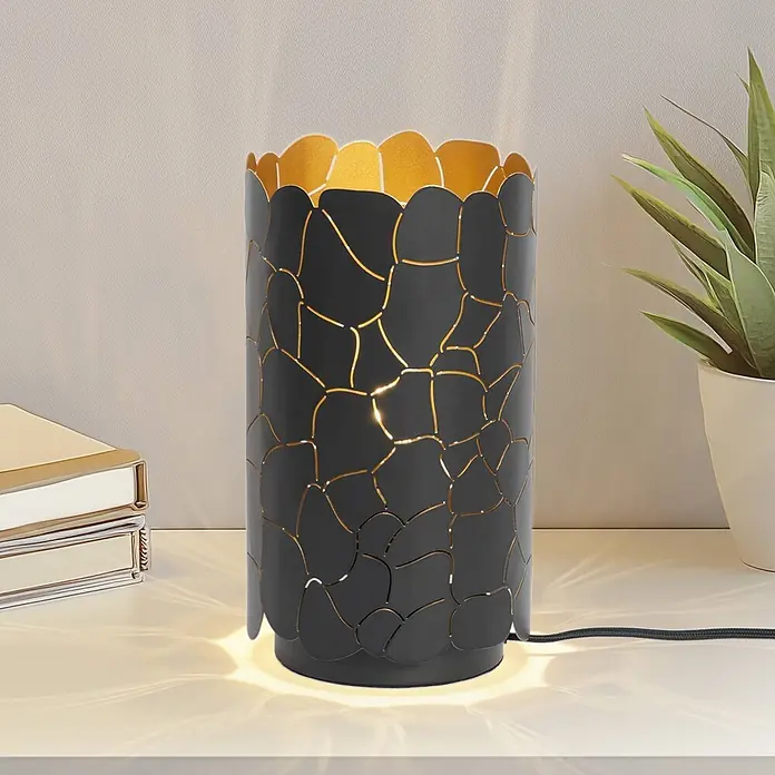 Lindby Tischleuchte Aralena - L x B x H: 15 x 15 x 26,5 cm, schwarz, E27 - Schwarze Metalltischleuchte mit organischen Lasercut-Mustern und goldener Innenseite, spendet stimmungsvolles Licht auf einem Regal.