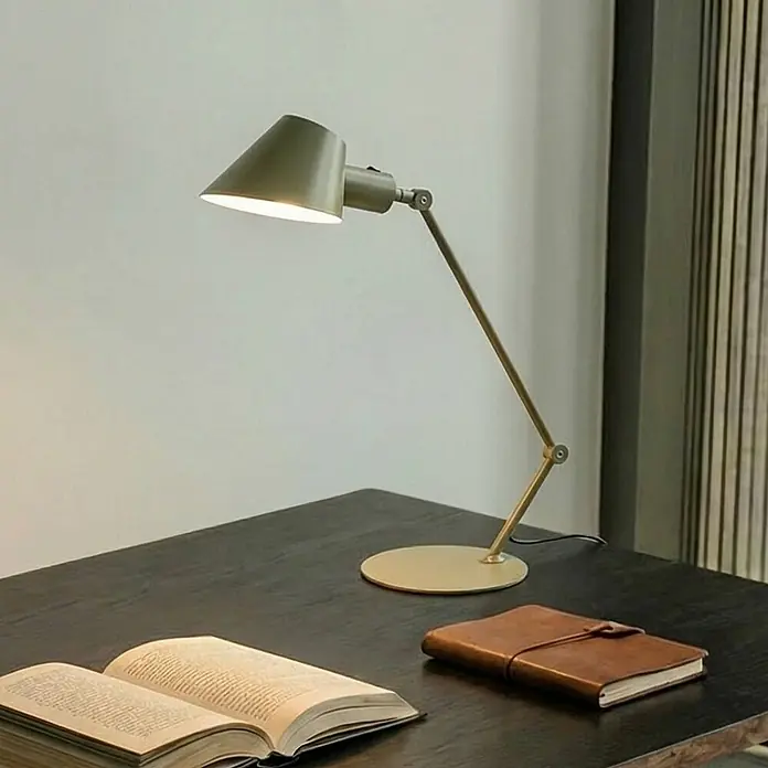 Lindby Tischleuchte Corali - grün, grün, E27 - Olivgrüne Schreibtischlampe mit verstellbarem Arm und konischem Schirm, beleuchtet einen dunklen Schreibtisch mit offenem Buch und Ledernotizbuch.