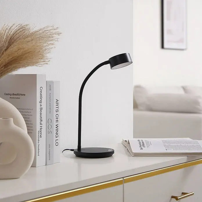Lindby Tischleuchte Maori - schwarz, schwarz - Schwarze Schreibtischlampe mit flexiblem Hals auf einem weißen Tisch, neben Büchern. Ihr verstellbarer Kopf spendet gerichtetes Leselicht.