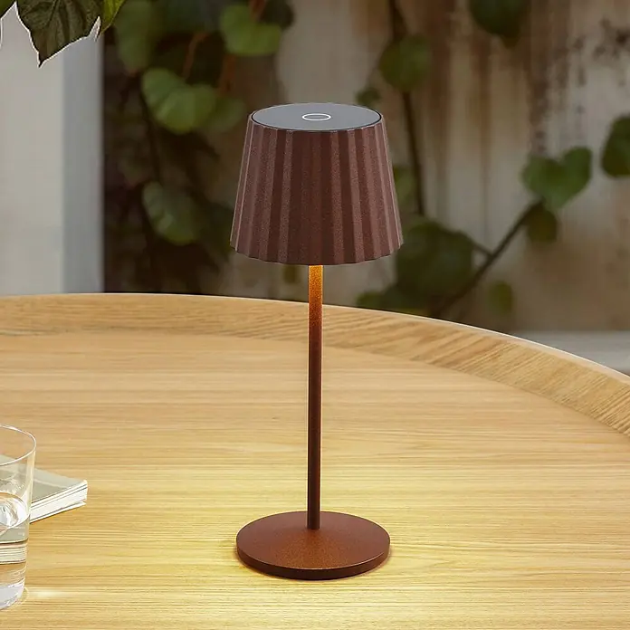 Lindby Tischleuchte Esali - L x B x H: 11 x 11 x 28,5 cm, braun / rost, braun / rost - Eine braune, geriffelte, tragbare Tischlampe mit schlankem Stiel steht auf einem hellen Holztisch und leuchtet warm.