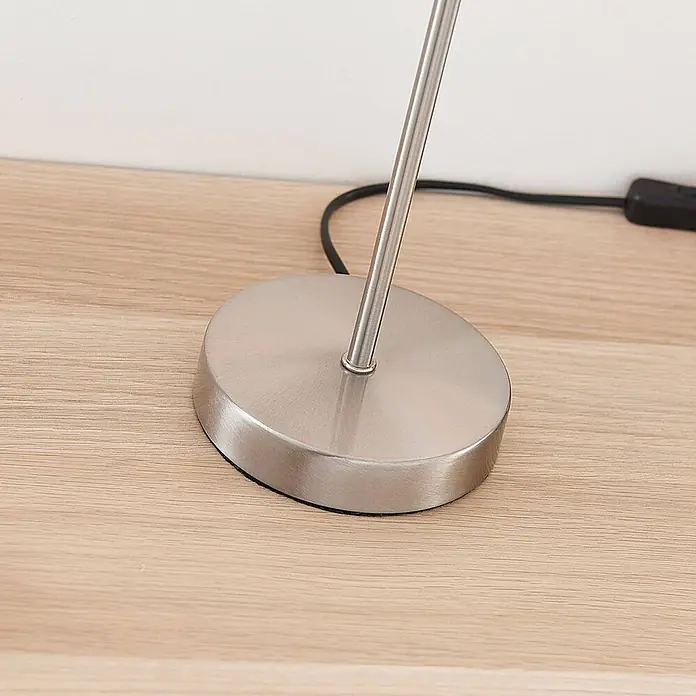 Lindby Tischleuchte Annatina - L x B x H: 20 x 20 x 48 cm, alu / grau / zink, weiß / opal, E27 - Ovale Lampenbasis aus gebürstetem Metall auf heller Holzoberfläche, mit einem schwarzen Netzkabel sichtbar.
