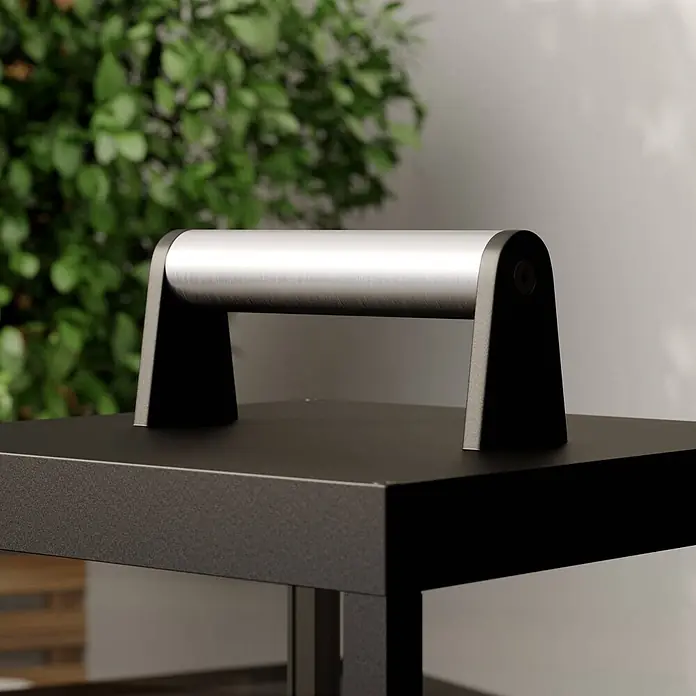 Lucande Tischleuchte Cube - schwarz - Eine Grillpresse mit gebürstetem Silbergriff und dunkelgrauem Unterteil, auf einer dunklen Fläche im Außenbereich.