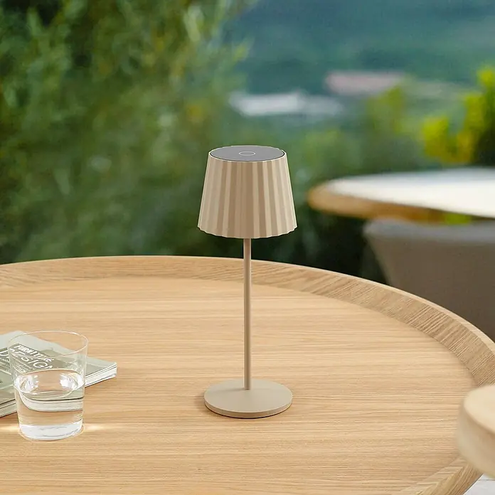 Lindby Tischleuchte Esali - creme / amber, creme / amber - Beige Tischleuchte mit plissiertem Schirm und schlankem Fuß, auf einem hellen Holztisch im Freien.